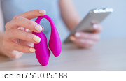 A woman synchronizes a modern curved clitoral vaginal vibrator with a smartphone. The girl has online sex using a toy. Стоковое фото, фотограф Михаил Решетников / Фотобанк Лори