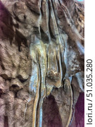 Close-up of the interior formations in a cave with dripstone structures created by thousands of years of mineralization. Long vertical formations and bizarre shapes on the walls create the impression of a stone waterfall. Soft light emphasizes the texture and natural colors of the rock. Стоковое фото, фотограф Анна Кривицкая / Фотобанк Лори