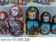 Brightly painted Russian nesting dolls displayed in a souvenir shop window. Large dolls are decorated with traditional ornaments, images of women in headscarves, and views of famous Russian churches. Smaller nesting dolls are visible in the background, creating an atmosphere of rich choice and national color. Стоковое фото, фотограф Анна Кривицкая / Фотобанк Лори