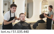 Young guy hairdresser stylist gives haircut to young male client in beauty salon. Стоковое видео, видеограф Яков Филимонов / Фотобанк Лори