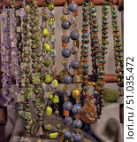 Close-up of beads and necklaces made of natural stones hanging on a wooden stand. The jewelry is made of amethyst, turquoise, amber, jadeite, lapis lazuli and other minerals. Each piece has a unique color, shape and texture that reflects the natural beauty of the stones. Стоковое фото, фотограф Анна Кривицкая / Фотобанк Лори