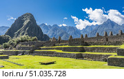 The famous archaeological complex of Machu Picchu. Stone terraces, a field with green grass, ruins of buildings against the background of mountains and blue sky. Majestic Wayna Pikchu. Стоковое фото, фотограф Вера Ивановна Кубарева / Фотобанк Лори
