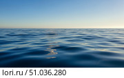 Travel background concept showing calm sea water surface with ripples under clear blue sky, peaceful ocean view at sunset for summer vacation or holiday theme. Стоковое фото, фотограф Павел Муравьев / Фотобанк Лори