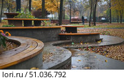 Explore a serene urban park with benches surrounded by blooming flowers under gentle rain, capturing the essence of autumn tranquility. Стоковое AI-видео, аниматор Данила Большаков / Фотобанк Лори