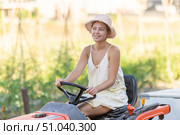 Young woman sits on minitractor and drives rural vehicle, performs loading work on farm. Стоковое фото, фотограф Яков Филимонов / Фотобанк Лори
