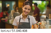 Asian woman is observed standing behind a restaurant counter, presumably taking orders or serving customers. Стоковое AI-видео, аниматор Данила Большаков / Фотобанк Лори