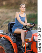 Young woman sits on minitractor and drives rural vehicle, performs loading work on farm. Стоковое фото, фотограф Яков Филимонов / Фотобанк Лори