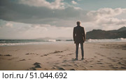 Business man stands atop a sandy beach, looking out at the sea. The sun glints off the water as waves crash gently onshore. Стоковое AI-видео, аниматор Данила Большаков / Фотобанк Лори