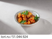 Crispy Korean chicken bites coated in glossy sweet chili sauce, sprinkled with sesame seeds and garnished with cilantro, served in a rustic ceramic bowl. Стоковое фото, фотограф Aleksandr Gavrilychev / Фотобанк Лори