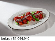 Crispy fried chicken wings coated in a rich Korean yangnyeom sauce, served on a white plate and garnished with sesame seeds and fresh cilantro. Стоковое фото, фотограф Aleksandr Gavrilychev / Фотобанк Лори