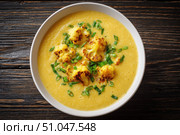 Cauliflower creamy soup with baked cauliflower florets on the top in a white bowl on a dark wood tabletop. Restaurant style dish. Hot, delicious plate of cream-of-cauliflower soup with melted cheese. Стоковое AI-изображение, AI-художник Марина Демидюк / Фотобанк Лори