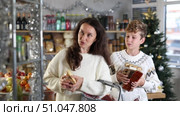 Adult woman buyer with son choosing different food in grocery store decorated for christmas. Стоковое видео, видеограф Яков Филимонов / Фотобанк Лори