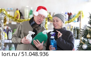 In Christmas decorated shop, mature spouses examines product and doubts choice, chooses kitchen cleaner spray and liquid detergent, study items properties in household department. Стоковое видео, видеограф Яков Филимонов / Фотобанк Лори