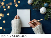 Woman's hand writing in empty notebook at the desk with Christmas decoration. Back to life, goal list. Plan, goals, checklist, idea concept. Top view, copy space. New Year. Blank White Paper Sheet. Стоковое AI-изображение, AI-художник Марина Демидюк / Фотобанк Лори