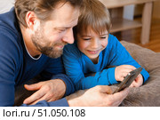 Father and son little boy laughing and using phone. They watching funny videos together, playing games on smartphone. Concept technology, smart phone addicted. Fun weekend activity. Modern fatherhood. Стоковое фото, фотограф Марина Демидюк / Фотобанк Лори
