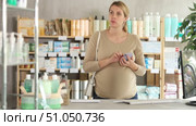 Attentive pregnant woman scrolling phone while looking for something in drugstore. Стоковое видео, видеограф Яков Филимонов / Фотобанк Лори