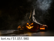 Three creepy Halloween grinning pumpkins glow in the dark among the fog. jack-o-lantern in a witch hat on a black background in smoke. Стоковое фото, фотограф Михаил Решетников / Фотобанк Лори