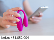 A woman synchronizes a modern curved clitoral vaginal vibrator with a smartphone. The girl has online sex using a toy. Стоковое фото, фотограф Михаил Решетников / Фотобанк Лори