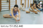 Positive young woman performing sitting stretches during warm-up in sports hall with others. Стоковое видео, видеограф Яков Филимонов / Фотобанк Лори