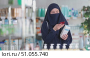 Attentive young female customer looking through barcode details of cream in drugsore. Стоковое видео, видеограф Яков Филимонов / Фотобанк Лори