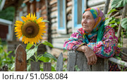Бабушка стоит у забора около своего дома в деревне. Grandmother is standing by the fence outside her house in the village. Стоковое AI-изображение, AI-художник Смирнова Светлана / Фотобанк Лори
