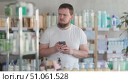 Young man with mobile phone choosing medicines and hygiene products in pharmacy. Стоковое видео, видеограф Яков Филимонов / Фотобанк Лори