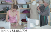 Female tailor draws a sketch of a fashion design against the background of a mature dressmaker. Seamstresses work in the workshop. Process of creating custom-made clothes and measurements. Стоковое видео, видеограф Яков Филимонов / Фотобанк Лори