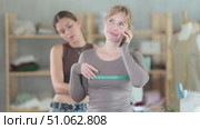 Woman tailor takes measurements from a client who is busy talking on the phone. Female client turned to fashion designers for tailoring clothes according to individual measurements. Стоковое видео, видеограф Яков Филимонов / Фотобанк Лори