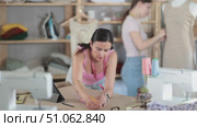 Using ruler and chalk, woman tailor draws dress diagram scheme on paper. Craftsman creates pattern for making dress. Companion worker in background with mannequin. Стоковое видео, видеограф Яков Филимонов / Фотобанк Лори
