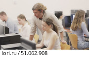 In classroom during computer courses, male teacher helps girl student complete difficult task, looks at monitor screen and corrects work. Mentor comments on students work, gives hints during task. Стоковое видео, видеограф Яков Филимонов / Фотобанк Лори
