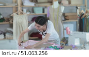 Young female fashion designer stands near a table in a sewing workshop and cuts fabric, checking the paper template. Process of tailoring clothes. Стоковое видео, видеограф Яков Филимонов / Фотобанк Лори