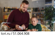 Young man with his son buying groceries from shopping list at grocery store. Стоковое видео, видеограф Яков Филимонов / Фотобанк Лори
