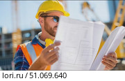 Construction worker reviewing plans at a busy site in bright sunlight. Стоковое AI-видео, аниматор Сергей Толмачёв / Фотобанк Лори