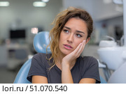Красивая молодая женщина сидит в современном стоматологическом кабинете, приложив руку к щеке от зубной боли. Стоковое AI-изображение, AI-художник Максим Коломыченко / Фотобанк Лори