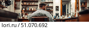Man sitting in barbershop chair facing mirror, surrounded by grooming products and tools in a classic interior, capturing grooming routine and stylish masculine atmosphere. Стоковое AI-изображение, AI-художник Катерина Бондарец / Фотобанк Лори