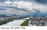 Urban landscape. Aerial view. Automobile bridge over the river. Green vegetation on the shores.There are many multi-storey buildings, a theater with a beautifully curved roof.Mountains against the sky. Стоковое фото, фотограф Вера Ивановна Кубарева / Фотобанк Лори