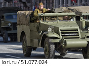 A historical military parade featuring World War II-era equipment. In the foreground is an American M3 Half-track armored personnel carrier, supplied to the USSR under the Lend-Lease program. The vehicle is painted olive green, with the tactical number L1-45-39 visible on the side. The driver is in the cabin and a serviceman in the Red Army uniform is at the Browning M2 machine gun mounted on the roof. The sides of the armored personnel carrier are equipped with protective armor panels, and the body is covered with a tarpaulin awning. Another war-era truck is visible in the background — probably a GMC CCKW, also painted in khaki. The action takes place on a city street, as part of a reconstruction or Victory Parade. (2015 год). Редакционное фото, фотограф Анна Кривицкая / Фотобанк Лори