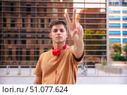 Happy young man raising fist in celebration wearing red headphones outdoors. Стоковое фото, фотограф Raquel Corcoles Mendez / Фотобанк Лори