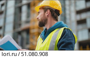 Construction worker reviews plans at building site during sunny day while wearing safety gear. Стоковое AI-видео, аниматор Сергей Толмачёв / Фотобанк Лори