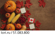 Autumn harvest scene with pumpkins, apples, corn, cranberries, and red maple leaves. Includes a Canadian flag and blank cards on a wooden surface. Стоковое AI-видео, аниматор Nart / Фотобанк Лори