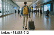 A young Caucasian man with short brown hair walks through an airport terminal, pulling a suitcase. The terminal is busy with travelers in the background. Стоковое AI-видео, аниматор Nart / Фотобанк Лори