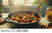A steaming pot of beef stew with carrots and potatoes sits on a wooden table. Sunlight streams through a window, illuminating the dish. Стоковое AI-видео, аниматор Nart / Фотобанк Лори