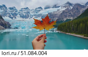 A hand holds a vibrant red maple leaf against a backdrop of a glacial lake and snow-capped mountains in Canada. The scene captures the essence of nature and national pride. Стоковое AI-видео, аниматор Nart / Фотобанк Лори