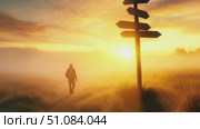 A silhouette of a person walking towards a signpost in a foggy landscape during sunrise. The scene conveys a sense of exploration and decision-making. Стоковое AI-видео, аниматор Nart / Фотобанк Лори