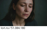 A young Caucasian woman with long brown hair covers her face with her hands, expressing distress or sadness. The background is dark and muted, enhancing the emotional tone. Стоковое AI-видео, аниматор Nart / Фотобанк Лори