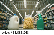 A shopping cart contains a bottle of milk, a bag of pasta, and a spray bottle. The scene is set in a grocery store aisle with shelves in the background. Стоковое AI-видео, аниматор Nart / Фотобанк Лори