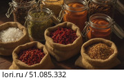 Various spices and herbs in jars and bags on a wooden surface. Includes salt, goji berries, and other colorful ingredients for cooking. Стоковое AI-видео, аниматор Nart / Фотобанк Лори