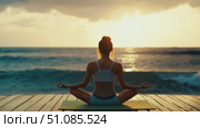 A young woman with long dark hair practices yoga on a wooden deck by the ocean at sunset. The scene conveys tranquility and mindfulness. Стоковое AI-видео, аниматор Nart / Фотобанк Лори