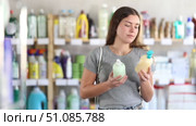 Female buyer holds liquid soap from different manufacturers in her hands and chooses between them while standing in a supermarket. Beautiful brunette girl buys antibacterial cream soap. Стоковое видео, видеограф Яков Филимонов / Фотобанк Лори