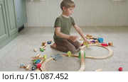 Cute little blonde child boy sitting on the floor playing with wooden toy train. Toddler kid plays railway. Made of natural materials. Birthday gift. Preschool employment. Brain, coordination exercise. Стоковое видео, видеограф Марина Демидюк / Фотобанк Лори